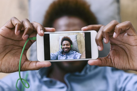 Junger afroamerikanischer Mann liegt auf dem Boden und macht ein Selfie, lizenzfreies Stockfoto