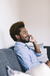 Junger afroamerikanischer Mann am Telefon, auf der Couch sitzend - EBSF000623