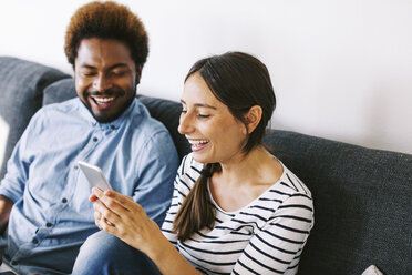 Young couple sitting on couch, using laptop and smart phone - EBSF000633