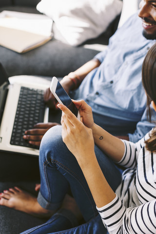 Young couple sitting on couch, using laptop and smart phone stock photo