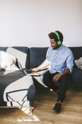 Young Afro American man sitting on couch, using laptop - EBSF000627