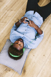 Young Afro American man lying on floor with headphones and smart phone - EBSF000629