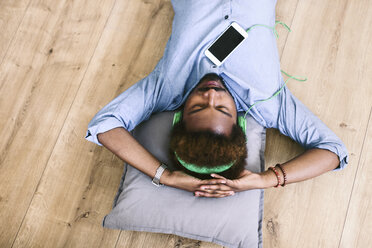 Young Afro American man lying on floor with headphones and smart phone - EBSF000635