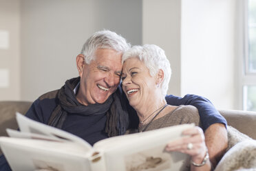 Senior couple sitting on a couch with photo album - ZEF005511