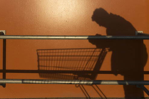 Shadow of a man leaning on empty shopping cart - ZMF000396