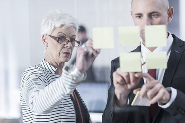 Colleagues discussing sticky notes on glass screen - ZEF005581