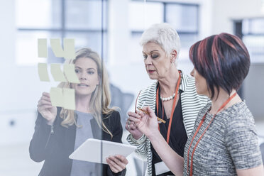 Colleagues discussing sticky notes on glass screen - ZEF005583