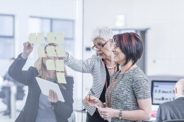 Colleagues discussing sticky notes on glass screen - ZEF005584