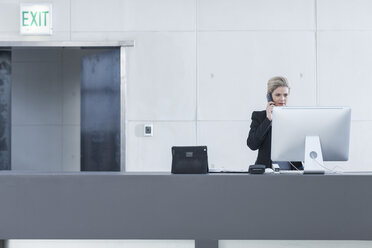 Woman behind reception desk in hotel lobby on the phone - ZEF005614