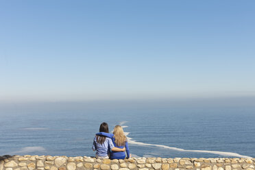 Südafrika, zwei Frauen sitzen Arm in Arm an einer Mauer an der Küste - ZEF005636