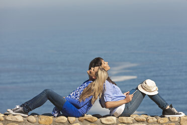 Südafrika, zwei glückliche Frauen sitzen Rücken an Rücken auf einer Mauer an der Küste - ZEF005638