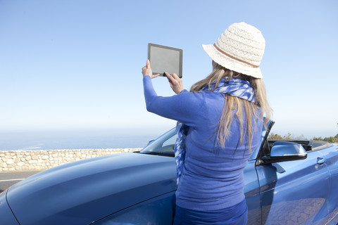 Südafrika, Frau an einem Cabrio, die mit einem digitalen Tablet fotografiert, lizenzfreies Stockfoto