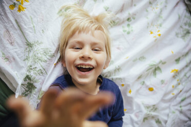 Lächelnder kleiner Junge auf dem Bett liegend, der die Hand zur Kamera ausstreckt - MFF001644