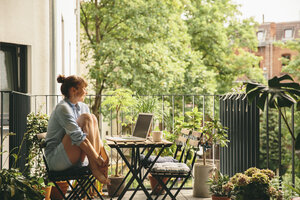 Lächelnde Frau schaut auf ihren Laptop auf dem Balkon - MFF001654