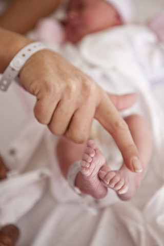 Die Hand einer Frau im Vergleich zu den Füßen eines Neugeborenen, lizenzfreies Stockfoto