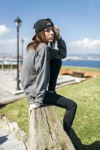 Spanien, Gijon, junge Frau sitzt auf Holzbalken, lizenzfreies Stockfoto