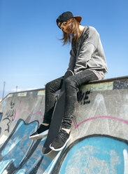 Weibliche Skateboarderin sitzt auf einer Mauer - MGOF000257