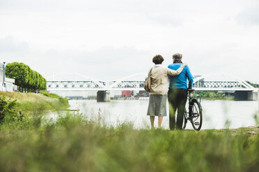 Back view of senior couple standing at water's edge with bicycle - UUF004495