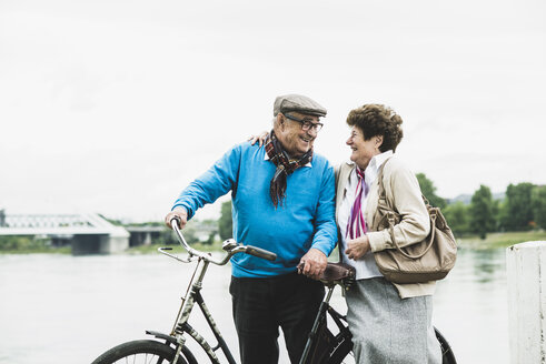 Glückliches älteres Paar mit Fahrrad am Wasser stehend - UUF004498