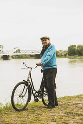 Porträt eines lächelnden älteren Mannes, der mit seinem Fahrrad am Ufer des Wassers steht - UUF004500