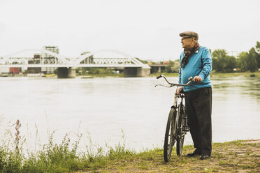 Senior man standing with his bicycle at water's edge - UUF004501