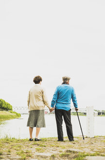 Back view of senior couple holding hands at water's edge - UUF004517