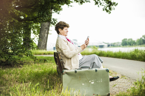 Ältere Frau sitzt auf einer Bank und benutzt ein Phablet, lizenzfreies Stockfoto