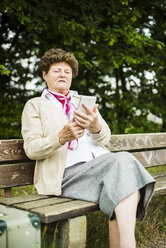 Ältere Frau sitzt auf einer Bank und benutzt ein Phablet - UUF004544