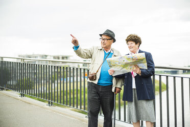 Senior couple with map standing on a bridge - UU004549