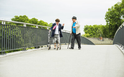 Älteres Paar mit Gehstock und Rollator auf einer Brücke - UUF004555