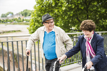 Laughing senior couple with walking stick and wheeled walker - UUF004560