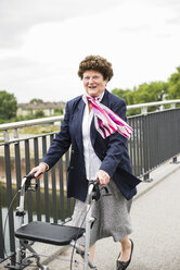 Lächelnde ältere Frau, die mit einer Gehhilfe auf Rädern geht - UUF004563