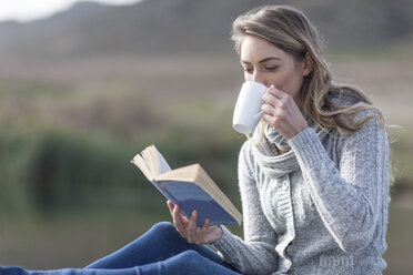 Frau mit Buch trinkt Kaffee auf einem Steg am See - ZEF006170