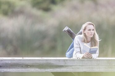 Frau mit Buch entspannt sich auf einem Steg am See - ZEF005778