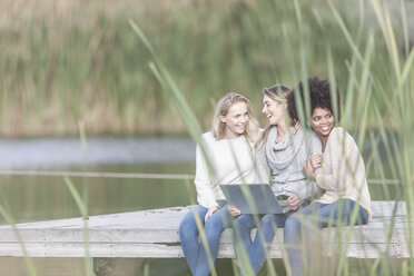 Drei Frauen mit Laptop entspannen sich auf einem Steg am See - ZEF005780