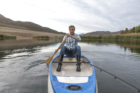 Porträt eines jungen Mannes mit Angelrute beim Paddeln auf einem See, lizenzfreies Stockfoto