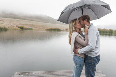 Küssendes Paar im Regen stehend mit Regenschirm - ZEF006219
