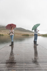 Paar steht im Regen auf der Holzpromenade mit Regenschirmen - ZEF006221