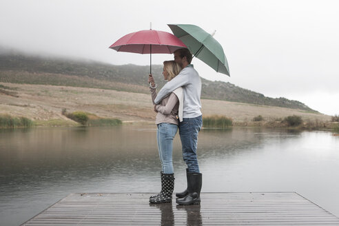 Couple standing in the rain on wooden boardwalk with umbrellas - ZEF006223