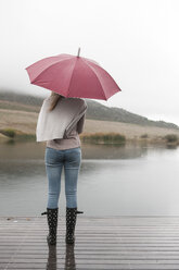 Rückenansicht einer jungen Frau, die mit einem Regenschirm im Regen steht - ZEF006225