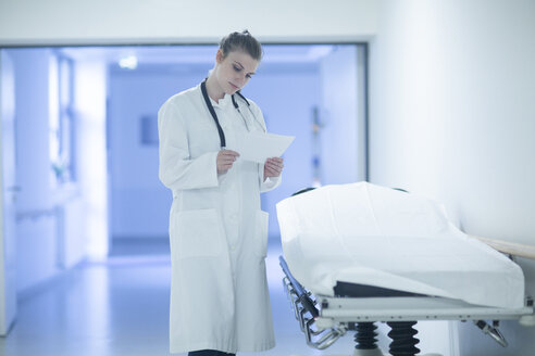 Young doctor on hospital floor reading document - SGF001651