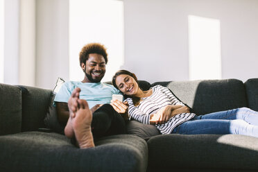 Young couple lying on couch looking at smart phone - EBSF000684