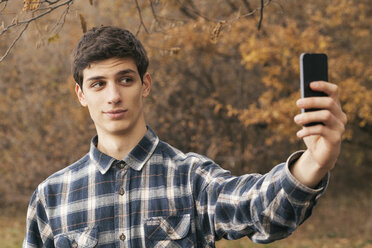 Porträt eines jungen Mannes, der ein Selfie mit seinem Smartphone in einem Park macht - BZF000160