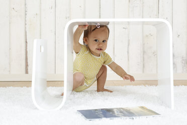 Baby-Mädchen hockt unter modernem Beistelltisch - DRF001649