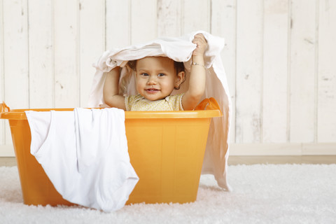 Kleines Mädchen in einem Wäschekorb sitzend, lizenzfreies Stockfoto