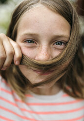 Porträt eines lächelnden Mädchens, das eine Haarsträhne unter der Nase hält - MGOF000276