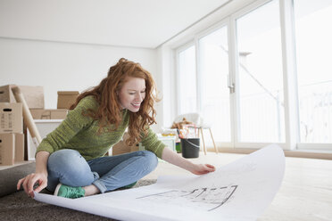 Young woman in new flat with cardboard boxes looking at ground plan - RBF002776