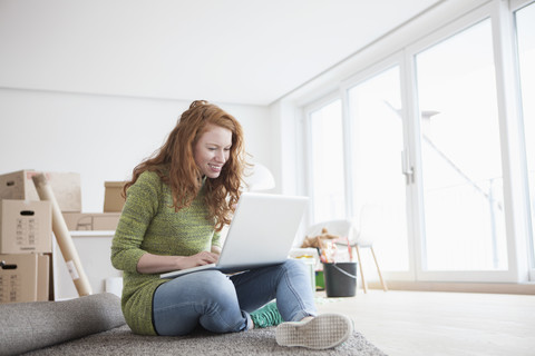 Junge Frau in neuer Wohnung mit Pappkartons und Laptop, lizenzfreies Stockfoto