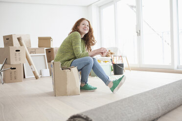 Junge Frau in neuer Wohnung sitzt auf einem Karton - RBF002778