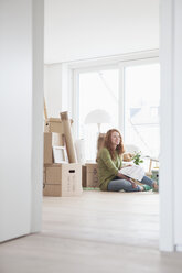 Junge Frau in neuer Wohnung mit Pappkartons und Blick auf den Grundriss - RBF002857